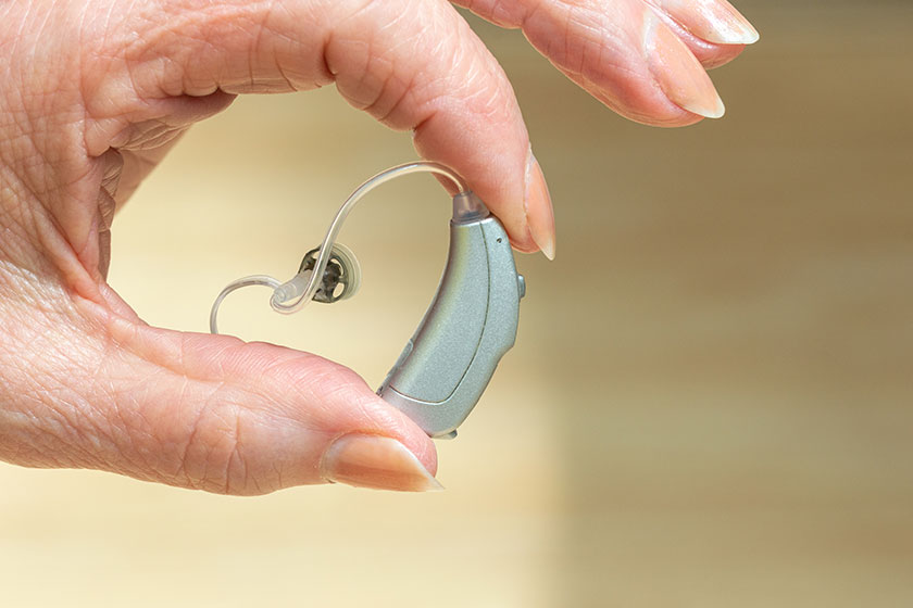 Behind The Ear hearing aid held between pensioners fingers.