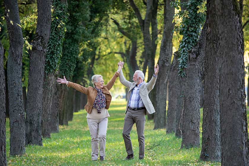 Senior couple celebrating life, love and happiness by raising arms and laughing in park