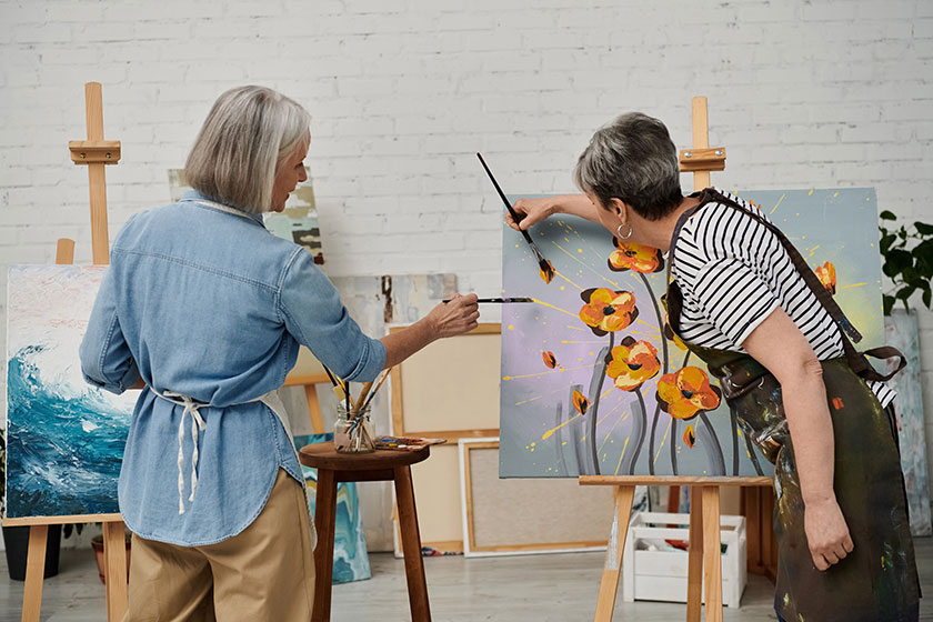 Two older women paint together in an art studio